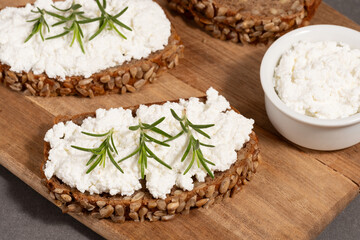 Delicious rye bread topped with creamy cheese and fresh herbs on a rustic wooden board