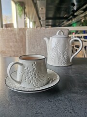 A white ceramic teacup with matching teapot on a modern table in a stylish cafe interior.
