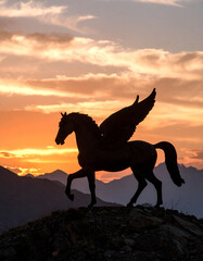Fototapeta premium A Kazakh tulpar statue (winged horse) silhouetted against a fiery sunset