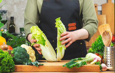 Chef cooking food in the kitchen. Cook holds halved Chinese cabbage. Wooden table, kitchenware,...