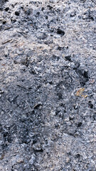Close-up view of a pile of white and black wood ash with charcoal remnants, showing rough texture and natural patterns after combustion.