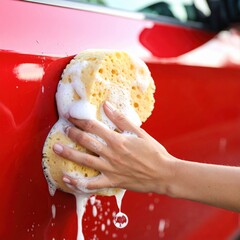 Close-up of hand washing car with yellow sponge and suds