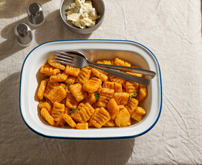 pumpkin gnocchi, garnished with fresh herbs in Enamel Bowl with Cutlery on Linen Tablecloth