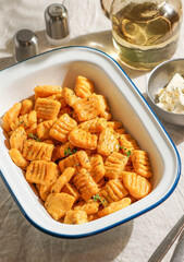 pumpkin gnocchi, garnished with fresh herbs in Enamel Bowl with Cutlery on Linen Tablecloth