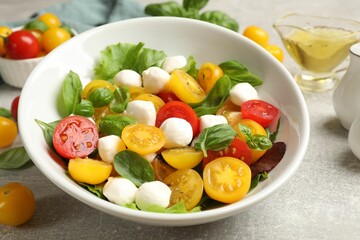 Tasty salad with yellow tomatoes, basil and mozzarella cheese on light grey table, closeup