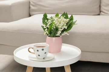 Bouquet of beautiful lily-of-the-valley and cup of tea on coffee table indoors