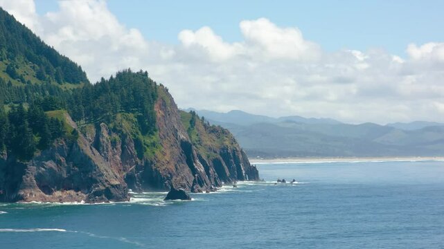 4K drone footage of Cape Falcon in Oswald West State Park. The cape juts into the Pacific, framed by evergreen forest and crashing ocean waves.