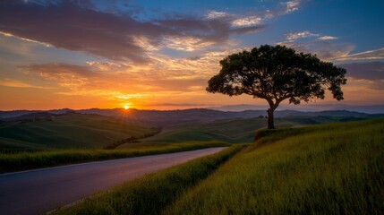 Fototapeta premium Enchanting sunset over rolling hills of Tuscany with vibrant orange, pink, blue, purple, and yellow sky hues, a winding road lined with green grass trees, a solitary tree casting long evening shadows.