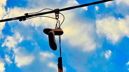 Old shoes hanging from a power line against a blue sky with clouds