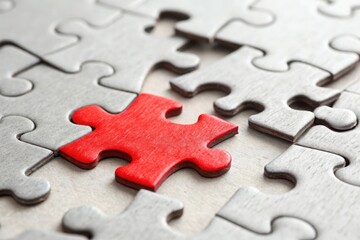 Fototapeta premium A red puzzle piece stands out among gray pieces on a textured surface