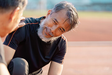 Supportive senior Asian man engaging in a wellness conversation with a friend on a track field.