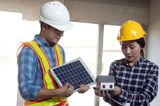 Male and female Asian engineers and technicians inspecting solar panels and house models, discussing sustainable energy solutions, showcasing innovation, safety, and environmental advancements.