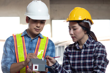 Male and female Asian engineers and technicians inspecting solar panels and house models, discussing sustainable energy solutions, showcasing innovation, safety, and environmental advancements.