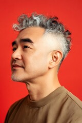 Fototapeta premium Conceptual art of style for aging men. Red solid background. A charismatic and fashionable male with a trendy look. Chic men's undercut haircut - midlife southeast asian man with curly hair.
