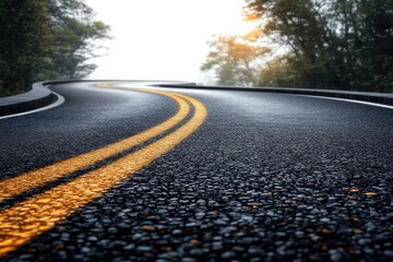 curved asphalt road with double yellow lines surrounded by trees under hazy sunlight