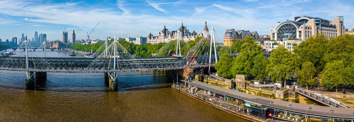 Panoramic aerial view of central London featuring the River Thames, Hungerford Bridge, Charing Cross Station, and iconic landmarks on a sunny day