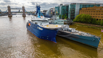 Obraz premium Moored ships on the River Thames near Tower Bridge and modern buildings on a cloudy day in London