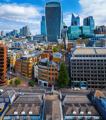 Modern skyscrapers and historic buildings in the City of London financial district under a bright blue sky, viewed from above