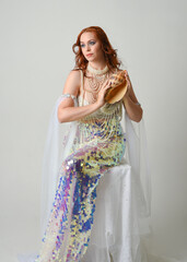 Fantasy studio portrait of a red-haired mermaid faery model wearing white pearl gown, fairytale...