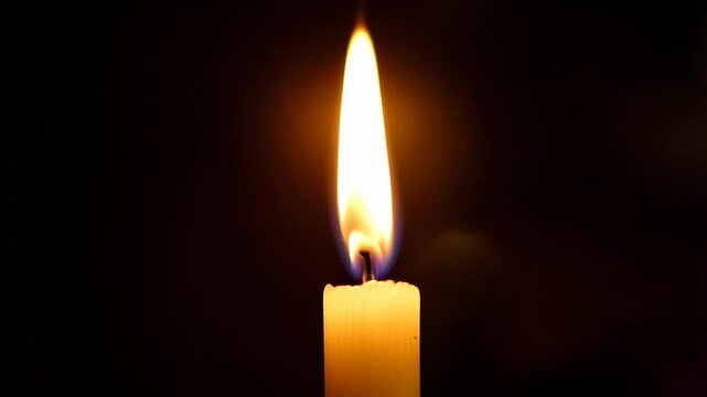 Close-up view of a single burning candle with a golden flickering flame on a black background, providing light in the darkness.