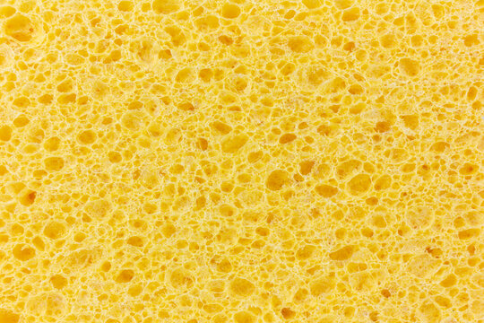 A close-up shot reveals the intricate, porous texture of a bright yellow cleaning sponge.