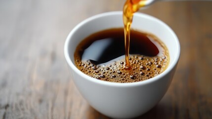 Close-up of hot black coffee being poured into a white cup on a wooden surface, with visible bubbles and steam conveying warmth and freshness