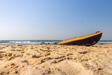 A red rubber swimming boat lies on a sandy beach, with the sea and clear blue sky in the background