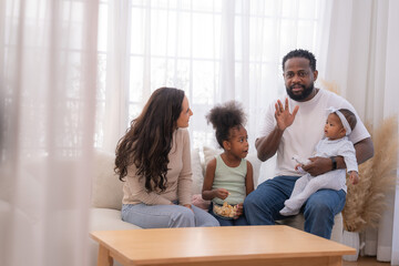 Fototapeta premium Happy family sitting together on a sofa, spending quality time and smiling while enjoying snacks at home in a warm and cozy living room.