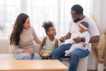 Happy family sitting together on a sofa, spending quality time and smiling while enjoying snacks at home in a warm and cozy living room.