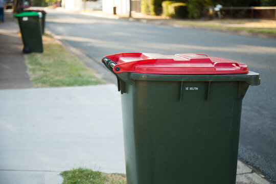 Red garbage bin beside road with green bin in background