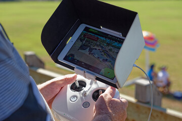 Man holding a white controller with aerial views visible flying his drone, uav, rpas