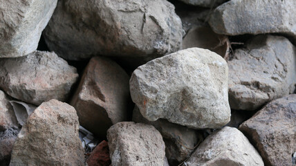 A textured gray stone wall background features a close-up of smooth granite pebbles, revealing a natural, hard pattern