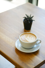 Cozy latte on a wooden table with a tiny plant