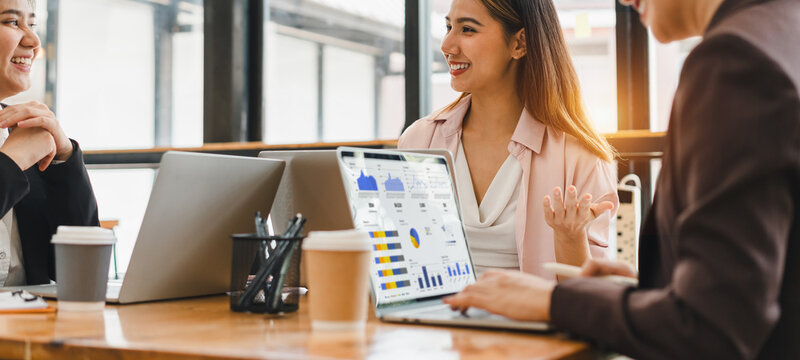 Business team meeting with laptops showing data analysis, young professionals discussing project in modern office, sunlight through windows creates positive atmosphere - Powered by Adobe
