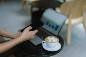 Businesswoman using smartphone on laptop screen in coffee shop