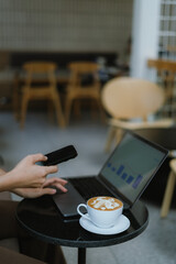 Businesswoman using smartphone on laptop screen in coffee shop
