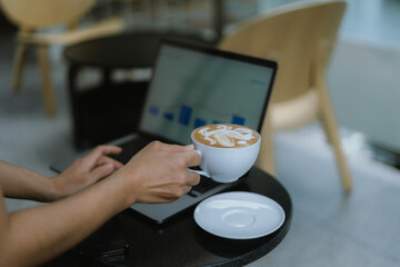 Freelance woman holding a cup of coffee and using a laptop