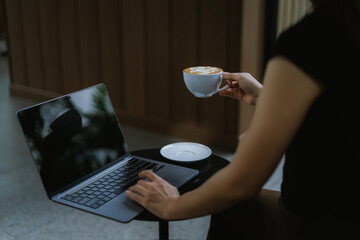 Freelance woman holding a cup of coffee and using a laptop