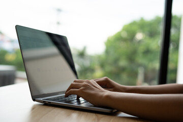 Woman's hands typing on laptop keyboard. Freelance or self-employed woman sitting at wooden desk with phone and smartphone.