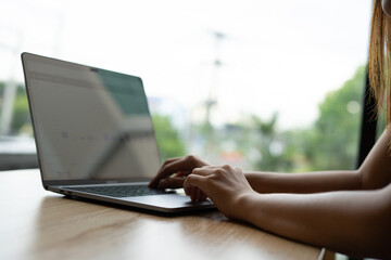 Woman's hands typing on laptop keyboard. Freelance or self-employed woman sitting at wooden desk with phone and smartphone.