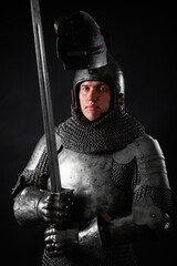 Portrait of a knight in full plate armor holding a sword posing isolated on a dark background