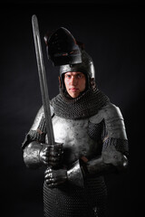 Portrait of a knight in full plate armor holding a sword posing isolated on a dark background