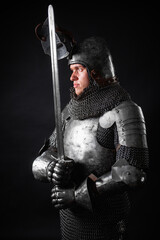 Portrait of a knight in full plate armor holding a sword posing isolated on a dark background