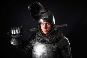 Portrait of a knight in full plate armor holding a sword posing isolated on a dark background