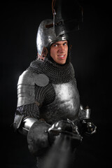 Portrait of a knight in full plate armor holding a sword posing isolated on a dark background