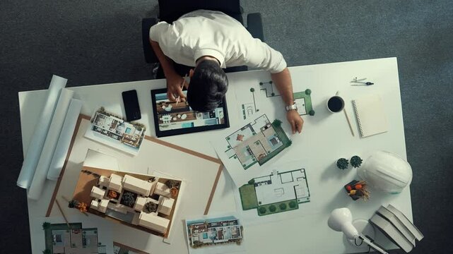 Top view of business man using tablet plan house design while sitting at meeting table with blueprint and equipment scatter around. Aerial view of civil engineer working at blueprint. Alimentation.