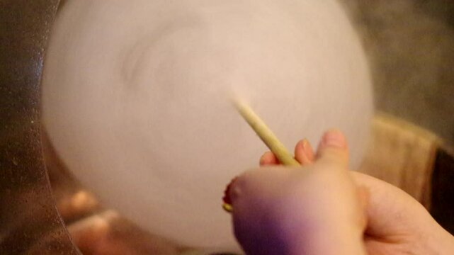 Making cotton candy spinning with a stick and adding sugar into candy floss machine closeup video