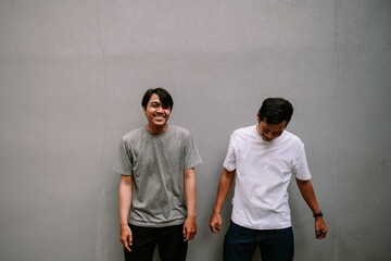 Two Young Men Posing Against Gray Concrete Wall, Wearing Casual Clothes