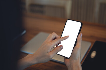 Mockup blank white screen mobile phone. Woman hand holding, using smartphone, finger touching on phone screen, working on laptop at coffee shop, mobile app design, online marketing, close up