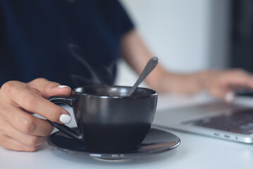Closeup, woman working on laptop computer, hand holding a cup of coffee on office table. remote work, online job, freelance lifestyle